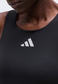 Gros plan d'une personne portant un haut noir sans manches avec un logo blanc Adidas centré sous l'encolure.