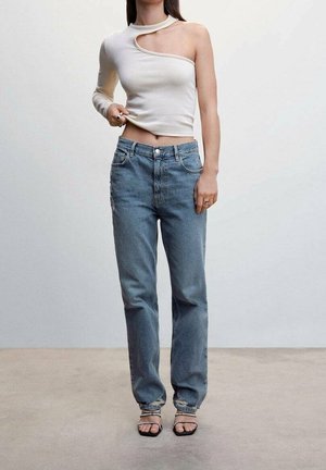 Bílý top na jedno rameno s unikátním výřezem; kombinovaný s světle modrými džíny s vysokým pasem; modelka má na sobě černé sandály na řemínky.