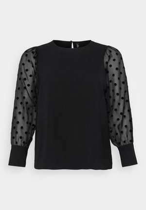 Haut noir avec un corps uni et des manches bouffantes transparentes à pois noirs. Encolure ronde avec une fermeture à bouton à l'arrière. Texture douce.