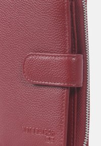 Rood leren portefeuille met een gestructureerd oppervlak, voorzien van een drukknoopsluiting, zichtbare stiksels en een zilveren rits aan de zijkant.