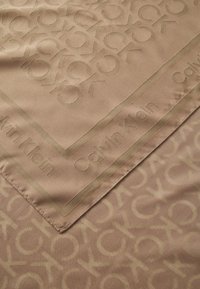 Sciarpa Calvin Klein in una tonalità beige chiaro, con un motivo tonale "CK". Texture liscia con un bordo che mostra il nome del marchio.