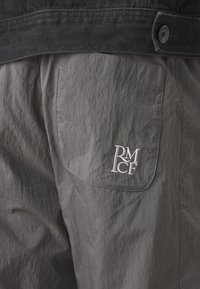 Pantalones cortos de tela gris con un acabado texturizado, que cuentan con un bolsillo trasero y un logotipo bordado en blanco "RM CF". Cintura oscura con cierre de botón.
