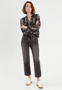 Blouse noire à fleurs avec des manches longues, associée à un jean gris taille haute et des baskets blanches décontractées. Un collier simple met en valeur le décolleté.