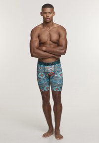 Boxer elasticizzati in un vivace turchese con motivi geometrici multicolori e motivi a ferro di cavallo; cintura elastica con marchio.