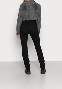 Pantalones negros ajustados combinados con una camiseta de manga larga de teñido anudado en gris. El atuendo presenta un diseño casual con una textura suave.