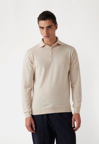 Polo shirt bej cu mânecă lungă, confecționat dintr-un material moale, având un guler clasic și închidere cu trei butoane, cu manșete și tiv cu bandă. 
