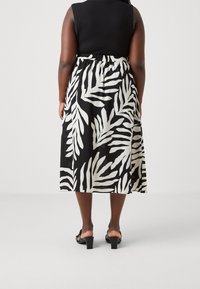 Jupe midi à motif de feuilles en noir et blanc avec une taille élastique, tissu fluide et ourlet arrondi, associée à des sandales à talons noires.