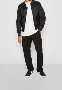 Svart bomberjacka med dragkedja, vit t-shirt under, svarta cargo byxor och svarta sneakers med vita accenter. Enkelt utseende, avslappnad passform.