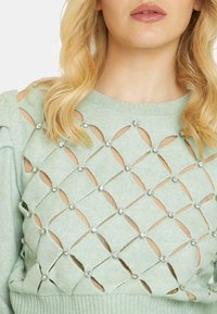 Maglione verde chiaro con motivo a rombi intagliato adornato con strass trasparenti, con polsini e orlo a costine.