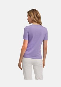 T-shirt viola a maniche corte realizzato in tessuto morbido. Presenta un collo rotondo e una consistenza liscia, abbinato a pantaloni bianchi.