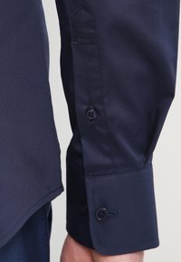 Marineblaues Hemd mit glattem Stoff, ausgestattet mit einem spitzen Manschette, zwei Knopfverschluss und dezentem Glanz.