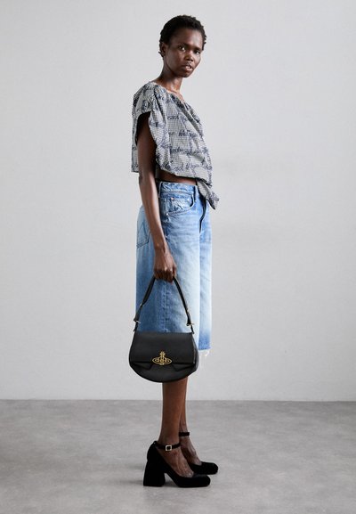 Mala de couro preta com detalhes em dourado, alça curta, forma arredondada; combinada com uma blusa cropped estampada e calções de ganga azul claro.