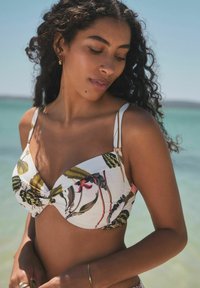 Weißes Bikinioberteil mit tropischem Pflanzen- und Blumenmuster, mit verdrehtem Vorderdesign, dünnen Trägern und goldfarbenen Akzenten.