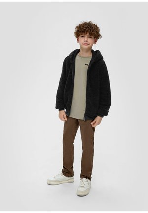 Veste zippée en polaire noire avec capuche, t-shirt olive clair avec imprimé "NON", pantalon marron et baskets blanches.