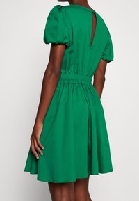 Grön kort klänning med puffärmar, elastiskt midjeband och en nyckelhålsdetalj bak. Tillverkad av ett mjukt tyg med en utsvängd kjol.