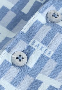 Tissu rayé bleu et blanc avec motif texte « BAKER » et deux boutons gris gravés « TED BAKER » cousus sur le vêtement.