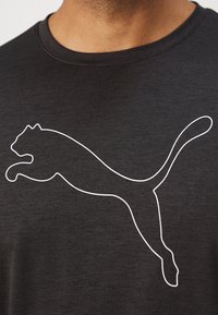 Tricou negru din bumbac, cu un logo în contur alb reprezentând o pisică săltând pe partea din față. Gât rotund, mâneci scurte și textură moale.