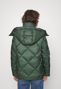 Grøn quiltet pufferjakke med hætte, der har et geometrisk diamantmønster og en glat, skinnende overflade.
