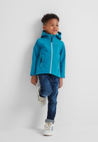 Turquoise hooded jacket with a zipper and two side pockets, paired with dark blue jeans and white sneakers featuring blue stripes.