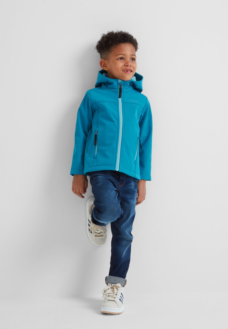 Turquoise hooded jacket with a zipper and two side pockets, paired with dark blue jeans and white sneakers featuring blue stripes.