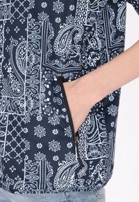 Top a fantasia navy con motivi paisley e floreali bianchi; include una tasca con zip e un tessuto testurizzato.
