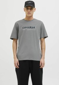Grå bomulds t-shirt med korte ærmer og rund hals, der har et blåt grafisk print med teksten "coredept." og "CREATIVE DEPT." på fronten.