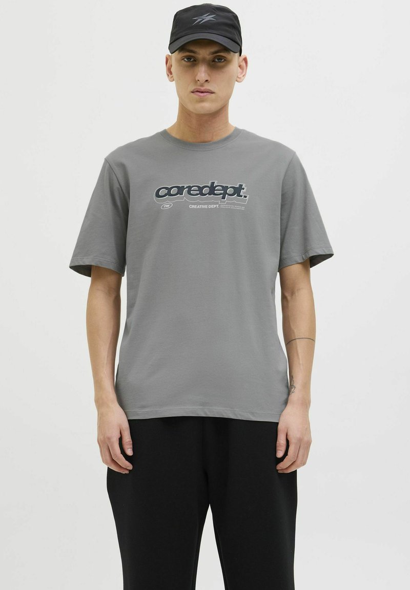 Grå bomulds t-shirt med korte ærmer og rund hals, der har et blåt grafisk print med teksten "coredept." og "CREATIVE DEPT." på fronten.