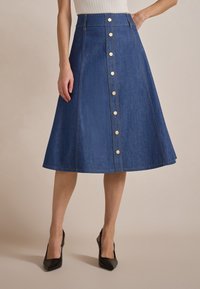 Denim A-linjekjørt med gullsnapplommer nedover foran, midtlangt, med synlig søm og jevn tekstur.