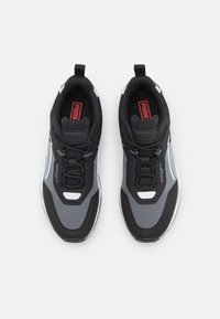 Black and gray athletic sneakers with mesh and synthetic materials, rounded toe, laces, and prominent brand logo on the tongue.