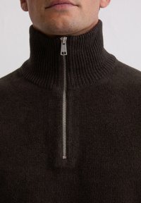 Brauner Pullover mit Reißverschluss aus geripptem Strickstoff. Mit hohem Kragen und silbernem Reißverschluss mit rechteckigem Zugtab.