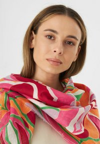 Kleurvolle sjaal van lichtgewicht stof met gedurfde bloemmotieven in roze, oranje en groen, met franjes aan de randen en een zachte textuur.