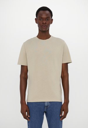 Beige cotton t-shirt with short sleeves and a crew neck, paired with blue denim jeans. Simple design, lightweight texture, no visible patterns.