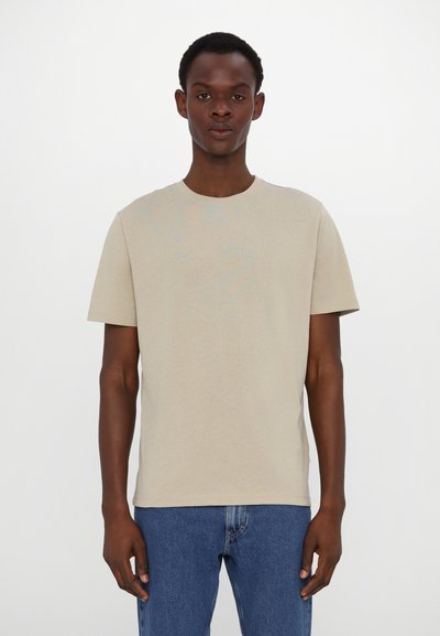 T-shirt en coton beige à manches courtes et col rond, associée à un jean en denim bleu. Design simple, texture légère, sans motifs visibles.