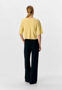 Gul ribbad stickad crop top med korta ärmar, i kombination med svarta vida byxor. Toppen har en rund halsringning och en strukturerad yta.