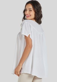 Blusa blanca, holgada, con mangas cortas y escote redondo, que presenta un diseño recogido en la parte trasera y está hecha de una tela suave y ligera.