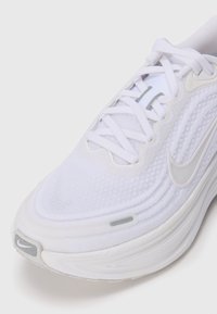 White athletic sneaker with mesh upper, lace-up design, and a gray Nike swoosh on the side and toe.
