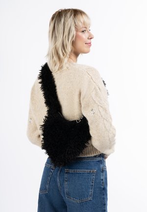 Geantă neagră pufoasă, în formă de inimă și cu o suprafață texturată, asociată cu un pulover bej deschis și blugi bleu cu talie înaltă.