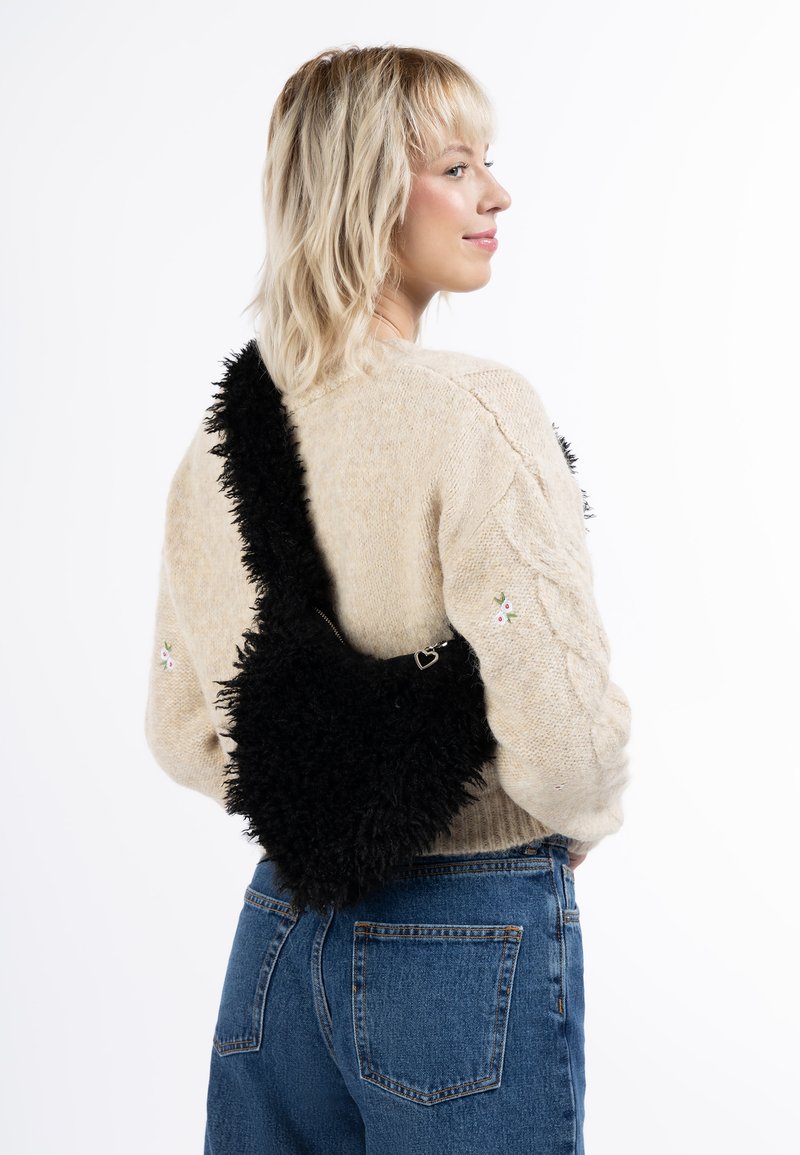 Geantă neagră pufoasă, în formă de inimă și cu o suprafață texturată, asociată cu un pulover bej deschis și blugi bleu cu talie înaltă.