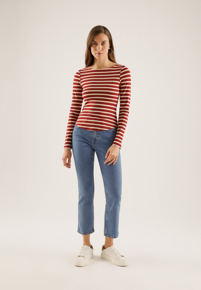 Rød og kremfargetstripete langermet topp kombinert med lyseblå caprijeans og hvite joggesko. Har en rund utringning og en tettsittende design.