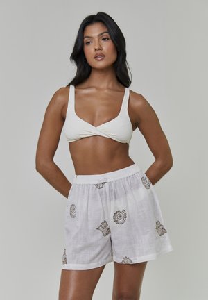 Hvide linnedshorts med brune skalmønstre, kombineret med en tekstureret cremefarvet bralette med krydsdetalje foran og brede stropper.