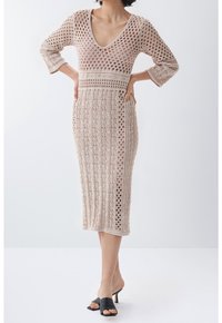 Robe en maille beige clair avec un col en V profond, manches trois-quarts, et un motif texturé ajouré ; longueur mi-mollet avec une silhouette ajustée.