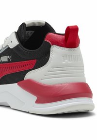Sneaker z czarną siateczkową cholewką, czerwonymi akcentami i teksturowaną białą podeszwą środkową. Pięta ma czerwony uchwyt i logo PUMA.