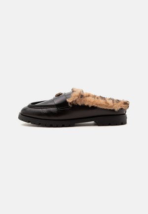 Mocassin noir en cuir à enfiler avec doublure en fausse fourrure marron et noire, semelle épaisse à crampons et boucle décorative sur le dessus, vu de côté.