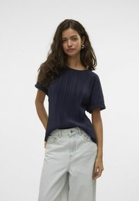 Marineblå plisseret top med korte ærmer, rund udskæring og afslappet pasform. Kombineret med lyseblå vide bukser. Glat tekstur, minimalistisk design.