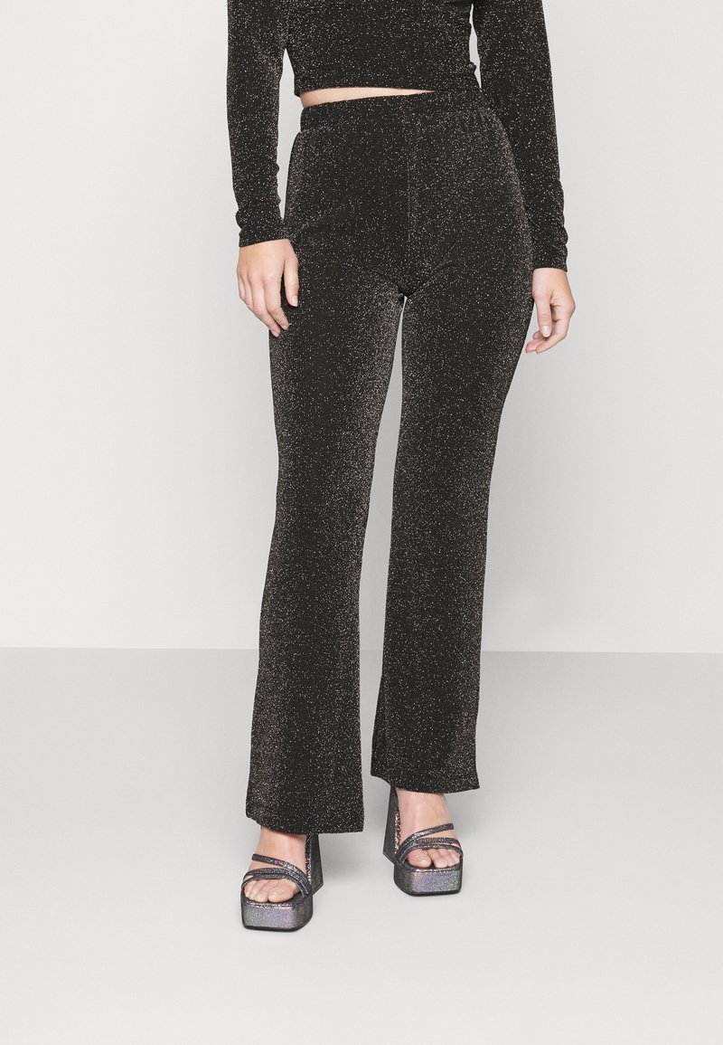 Svarta glittrande byxor med en utsvängd design, hög midja och slät yta, ihop med klumpiga blockklack-sandaler.