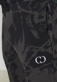 Zwarte en grijze joggers met een patroon, gemaakt van zachte katoen, met een trekkoordtaille en een witte geborduurde logo op het linkeronderbeen.
