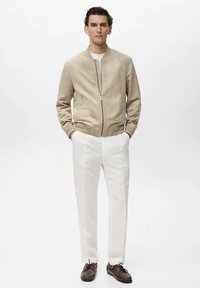 Jachetă bomber bej din suedă cu închidere cu fermoar, pantaloni albi slim-fit și pantofi maro din piele; design simplu cu caracteristici minimaliste.