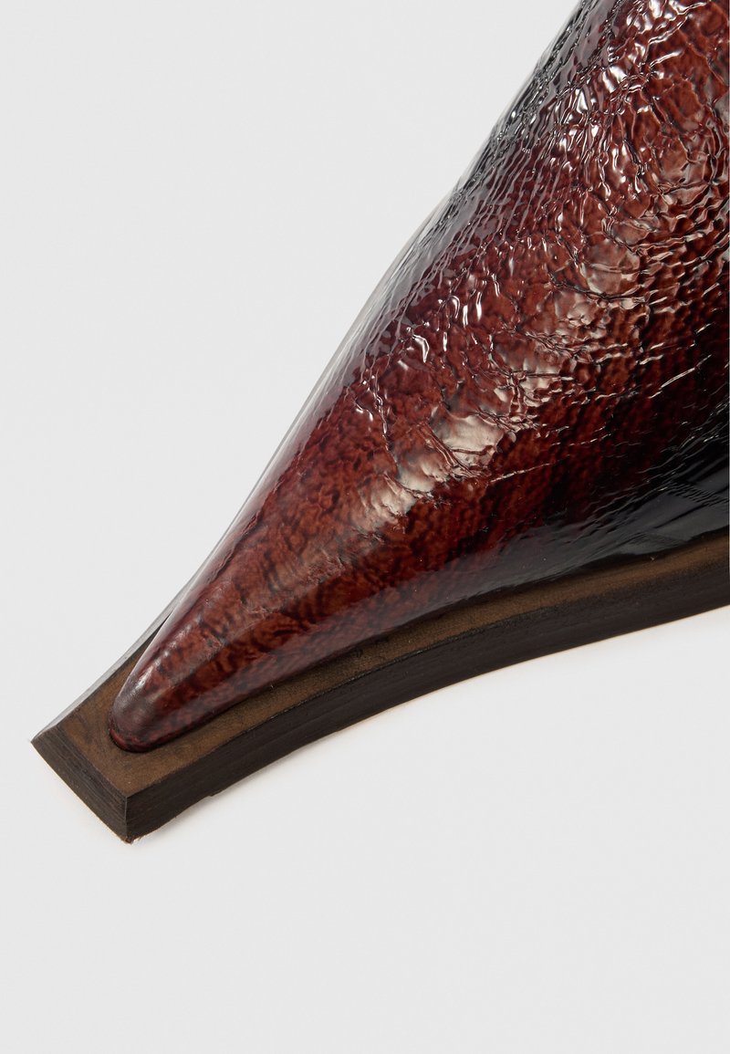 Zapato marrón puntiagudo con una superficie texturizada y brillante que recuerda a la piel de cocodrilo. Cuenta con una suela de madera con una ligera curva.