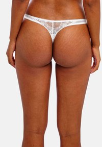 String en dentelle blanche avec motif floral, doté d'une taille fine et d'un tissu transparent, mettant en valeur un design délicat et une texture douce.