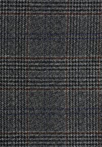 Tissu à carreaux gris avec un tissage texturé. Les motifs comprennent des lignes sombres et claires avec des accents rouges et bleus, créant une apparence à carreaux.